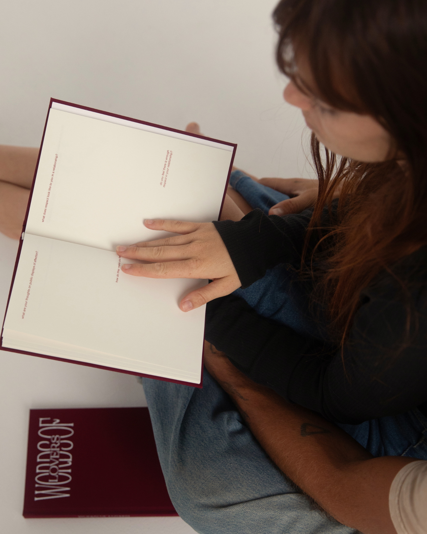 A person holding an open book with blank white pages, with the closed book showing the title 'WORDS OF' in white on a dark red cover placed below it.