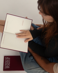 A person holding an open book with blank white pages, with the closed book showing the title 'WORDS OF' in white on a dark red cover placed below it.