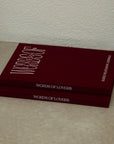 Two dark red hardcover books titled 'Words of Lovers' stacked on a light beige floor against a textured off-white wall.