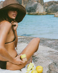 Woman applying sunscreen on a rock by the water