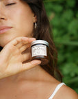 Woman holding a jar of Sol Medicinals Heal All Salve in front of a green blurred background